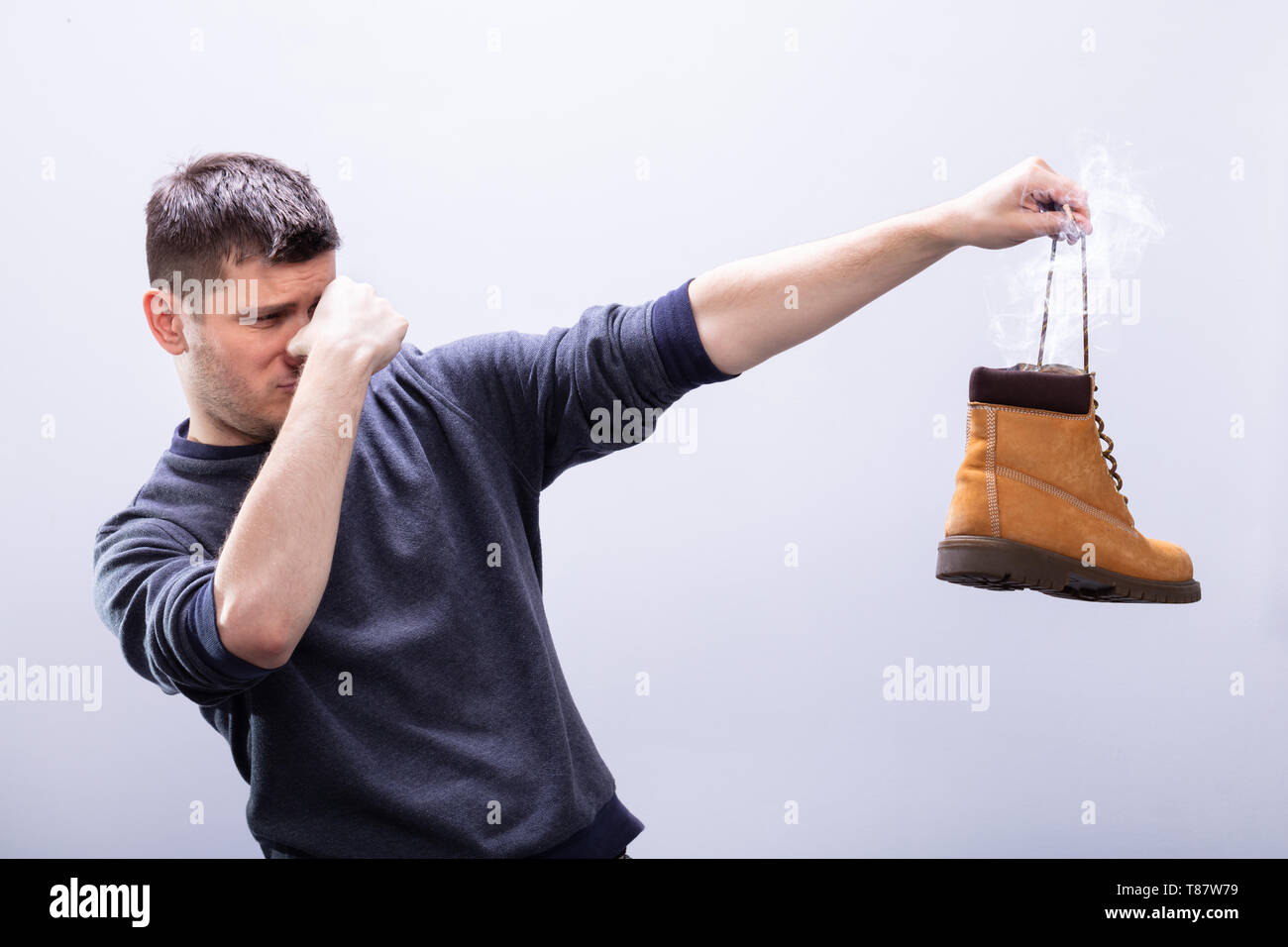 Close-up di un uomo che copre il suo naso tenendo Stinky calzatura contro uno sfondo bianco Foto Stock