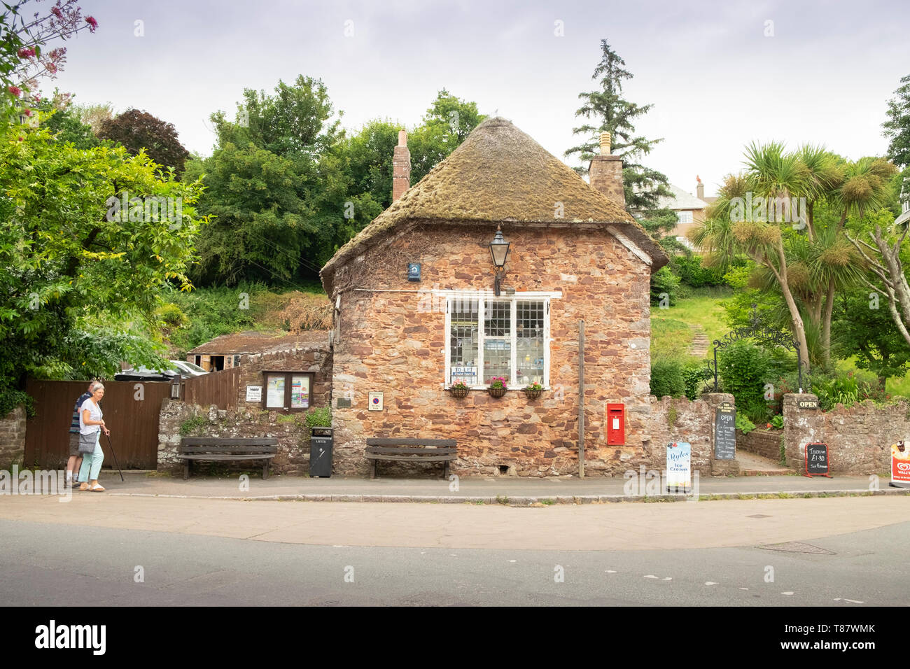 Cottage con il tetto di paglia convertito al villaggio tradizionale tourist shop nel villaggio di Cockington,Devon, Inghilterra, Regno Unito. Due anziani sono passato a piedi Foto Stock
