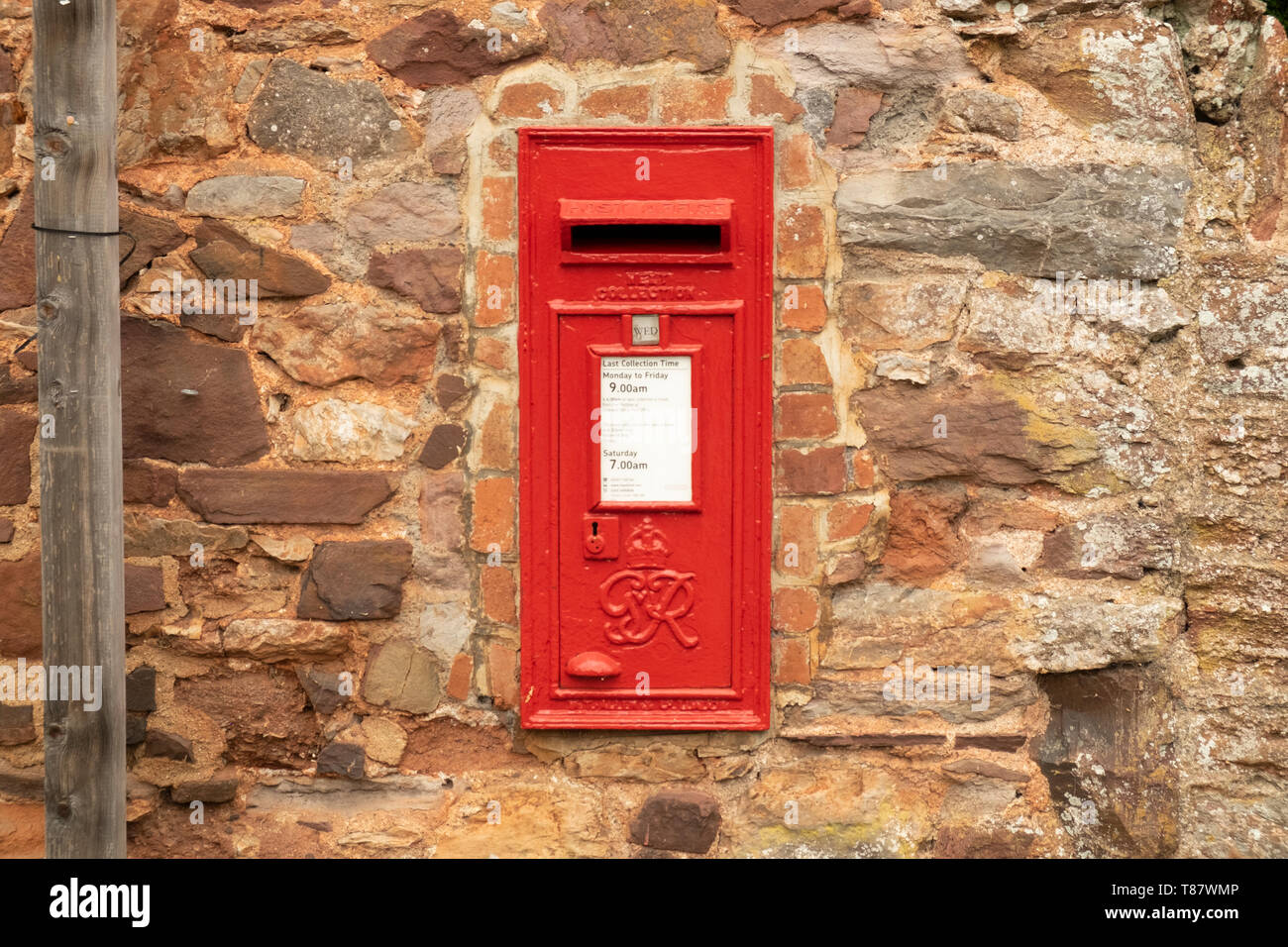 Rosso casella postale nel muro di pietra nel villaggio di Cockington,Devon, Inghilterra, Regno Unito Foto Stock