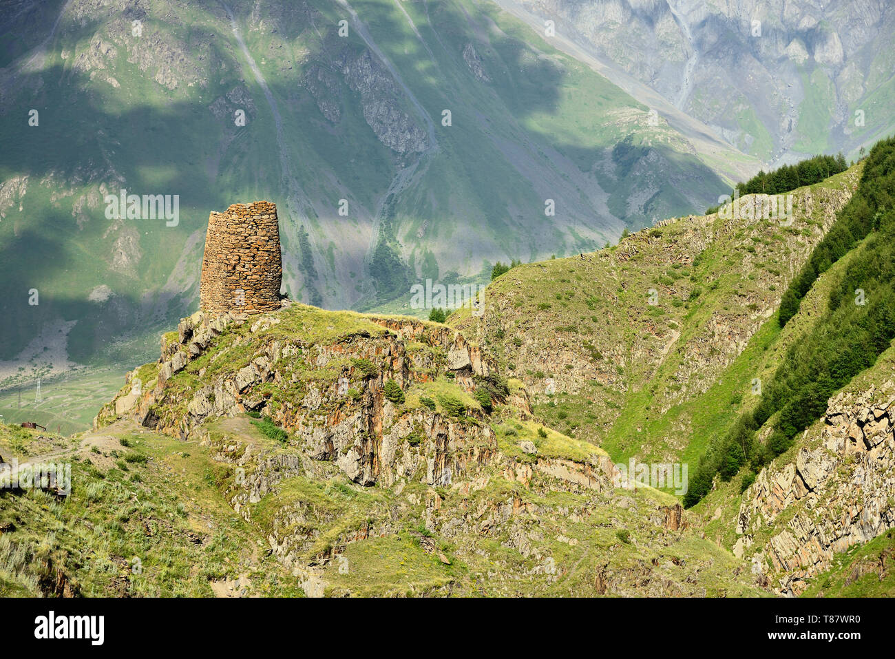 La vista sulla torre di difesa sulla rotta di Tsminda Sameba la Chiesa georgiana si trova sulla verde collina sopra la città Stepantsminda. Foto Stock