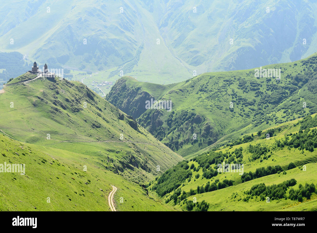 Il Tsminda Sameba la Chiesa georgiana si trova sulla verde collina sopra la città Stepantsminda. Percorso con una vista dal pass Sabertse Santuario e dal tr Foto Stock