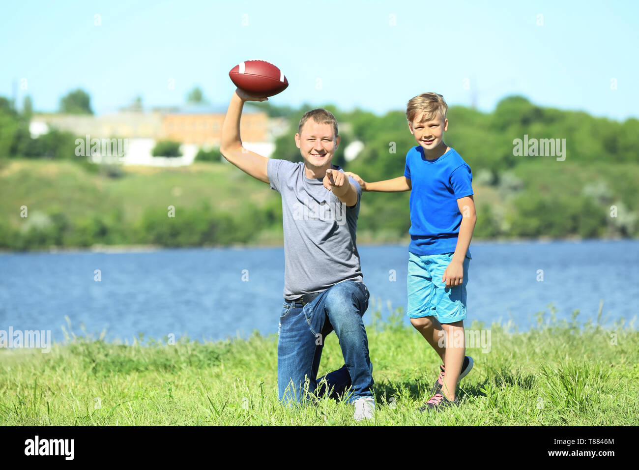 Felice di padre e figlio con palla da rugby vicino al fiume Foto Stock