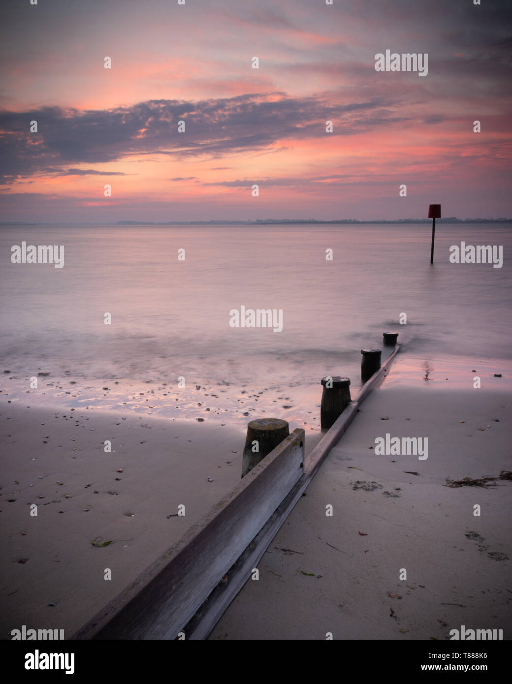 Un mare di legno marcatore o pennelli durante una tranquilla rosa sunrise su di una spiaggia di sabbia Foto Stock
