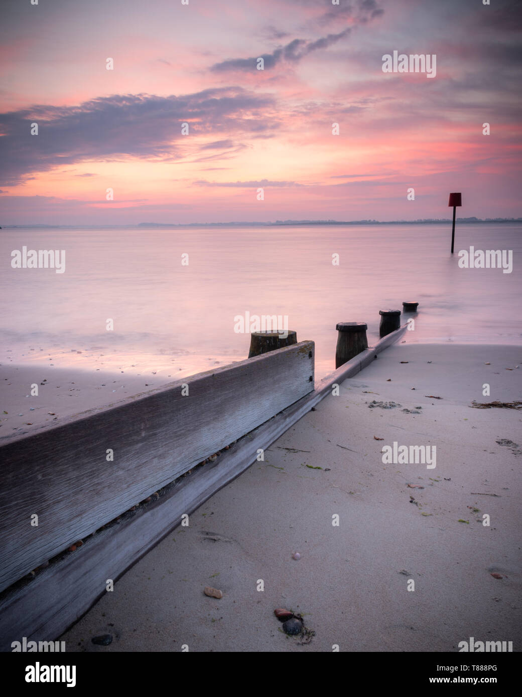 Un mare di legno marcatore o pennelli durante una tranquilla rosa sunrise su di una spiaggia di sabbia Foto Stock