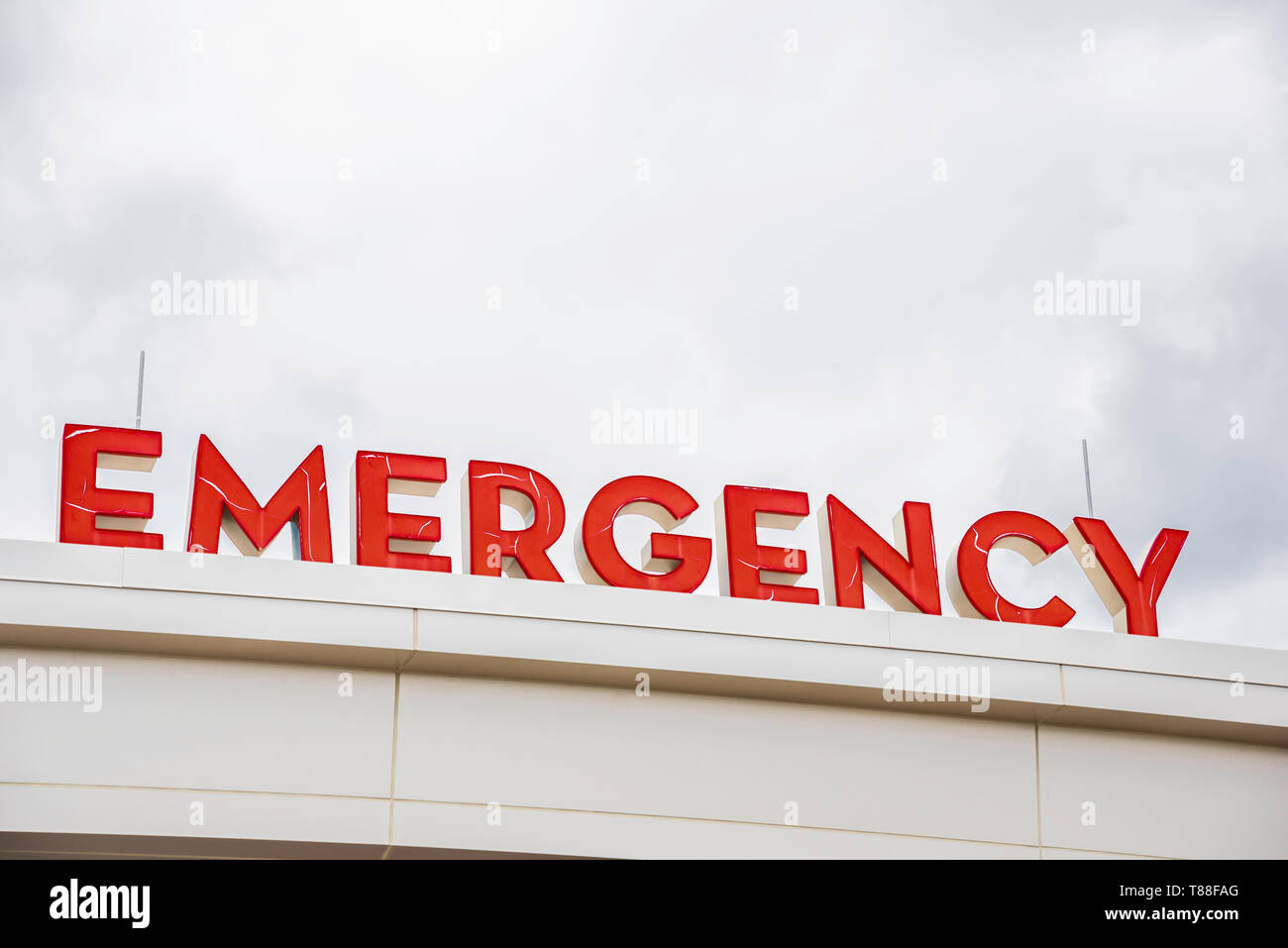 Un prominente red 3D tutte maiuscole emergenza illuminati segno direzionale e un marcatore appollaiato sulla tenda e la tettoia dell'ospedale principale entrata. Foto Stock