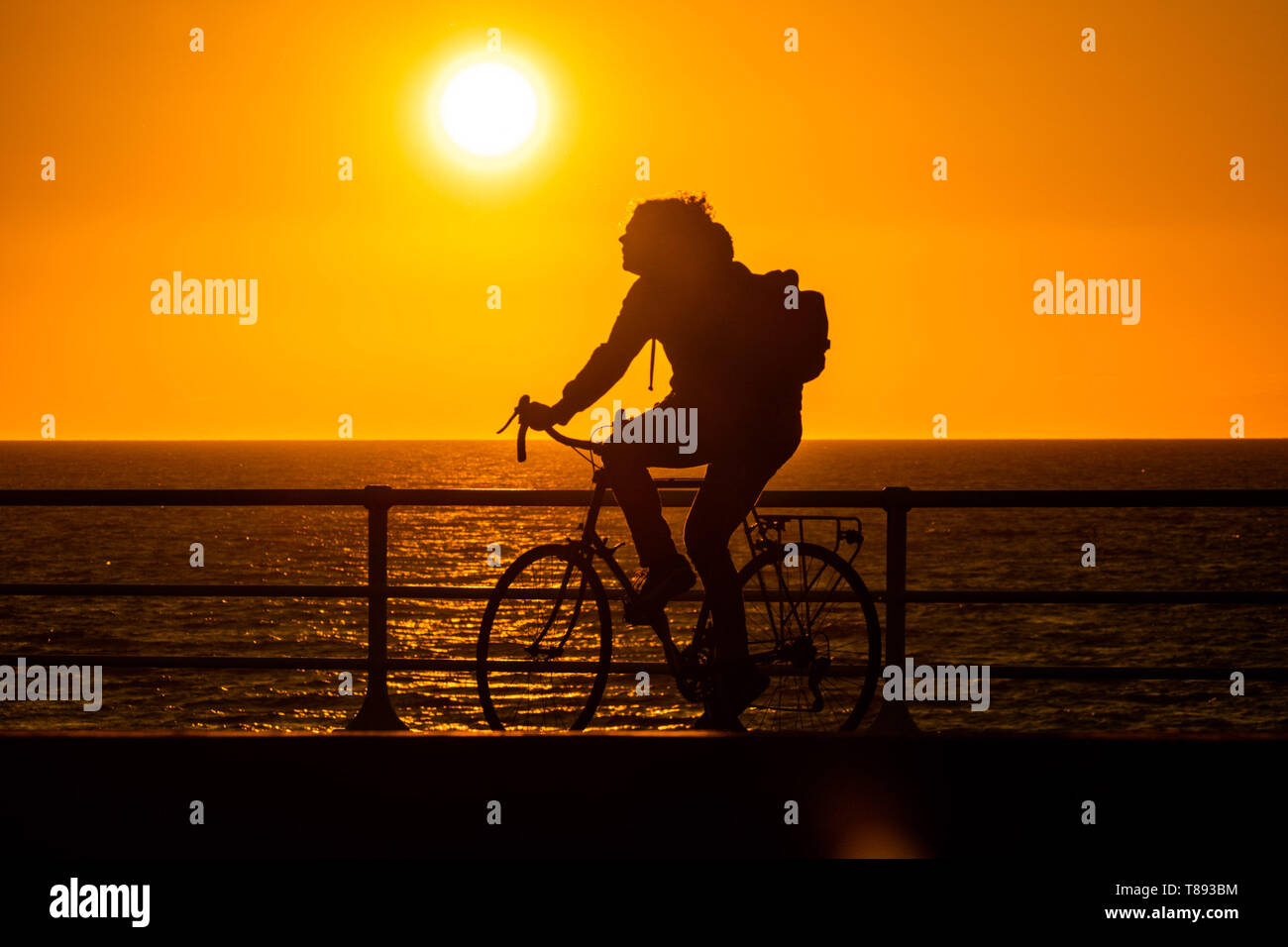 Aberystwyth Wales UK, Sabato 11 Maggio 2019 UK Meteo: un uomo che si stagliano contro il glorioso sole di setting come egli cicli lungo la passeggiata in Aberystwyth su Cardigan Bay costa, West Wales. Il tempo viene impostato per ottenere ancora più calda la prossima settimana dopo come periodo di inquieta freddo. Photo credit Keith Morris / Alamy Live News Foto Stock