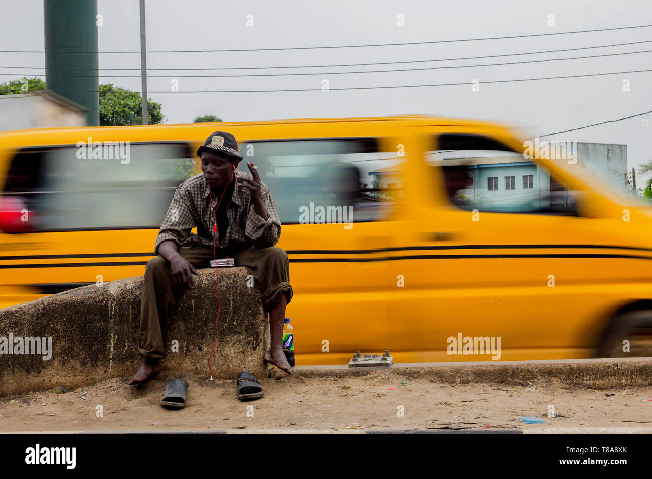 Un uomo senza tetto siede e fuma nel mezzo di un'autostrada a Lagos, Nigeria. Foto Stock