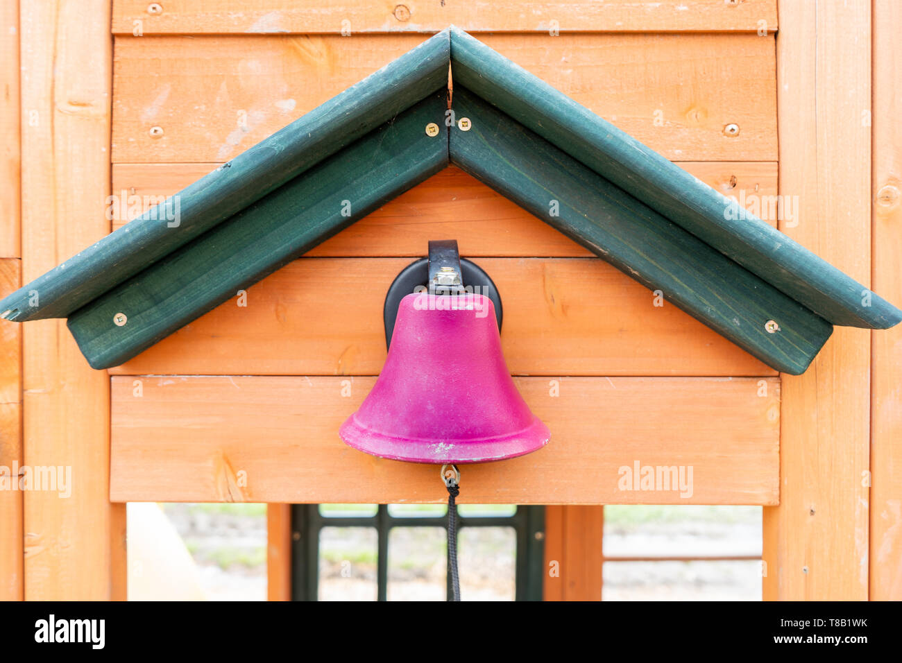 Far finta rosa Campanello scuola su un parco giochi in legno per esterni, con una stringa per rendere il ding dong di rumore, mentre i bambini partecipano in gioco all'aperto. Foto Stock