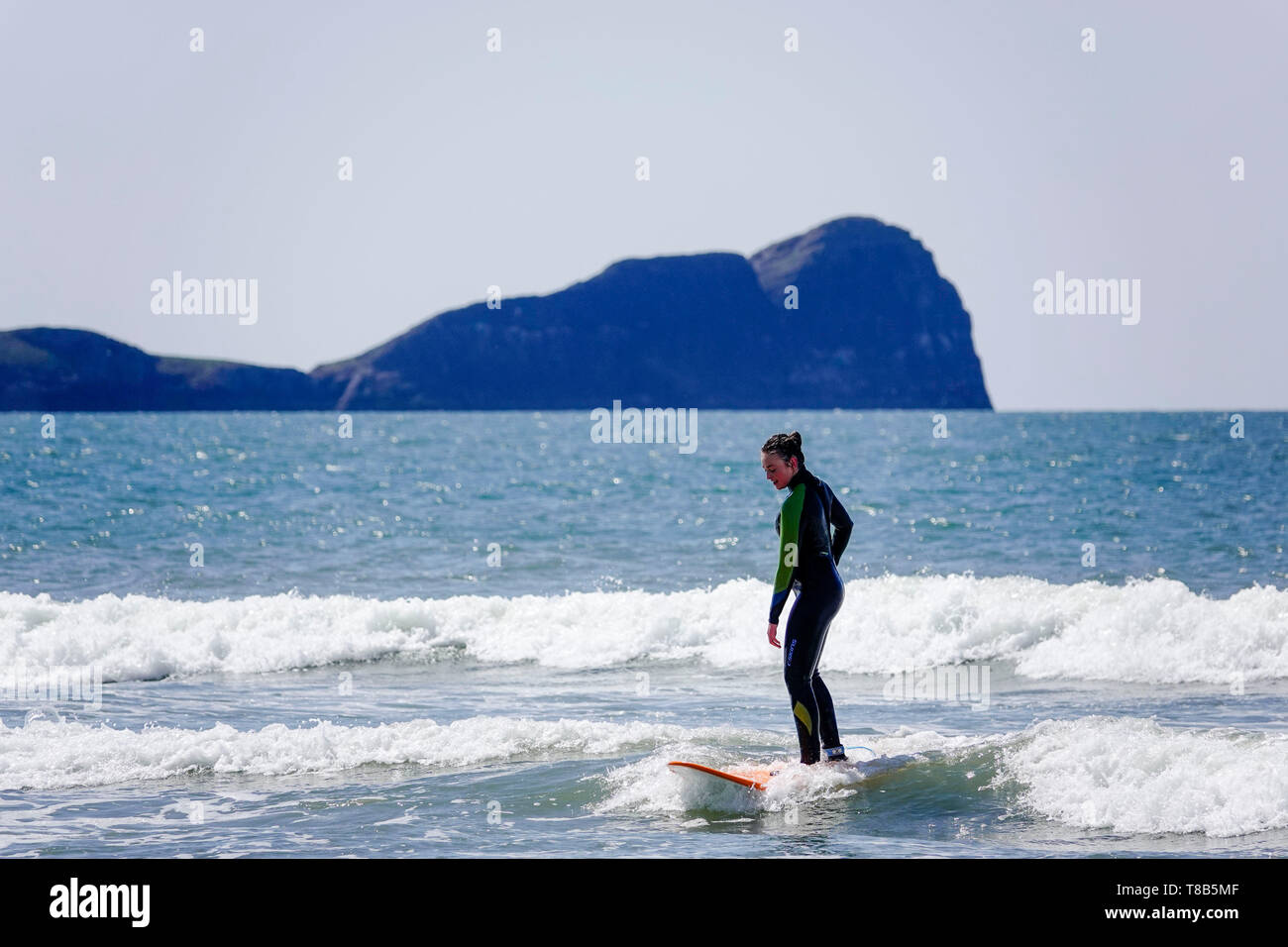 Giovane donna surfer a Llangennith beach, Penisola di Gower. Nella foto sullo sfondo del worm testa isola di marea. Foto Stock