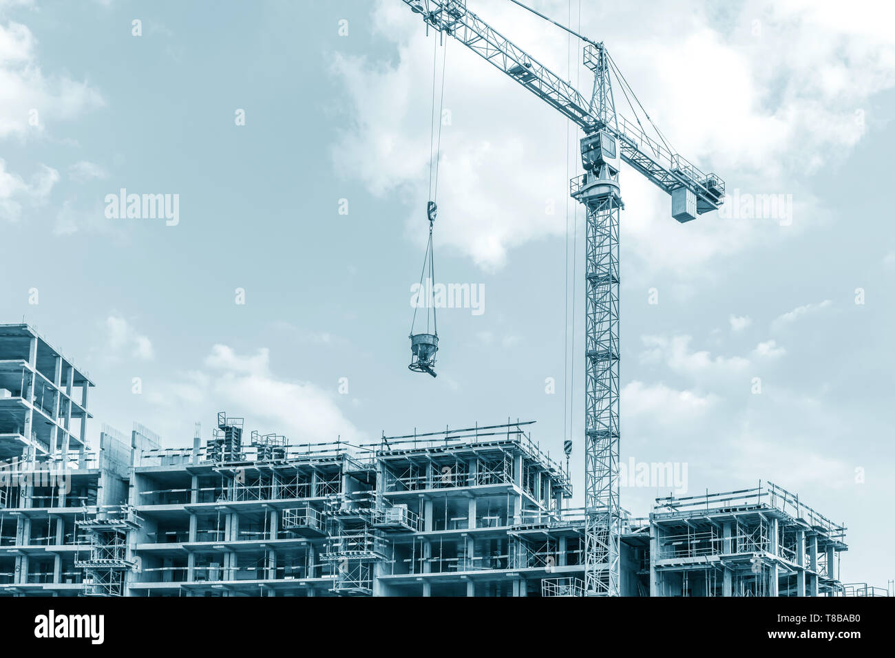 Edificio residenziale in costruzione e alta gru a torre contro il cielo blu sullo sfondo Foto Stock