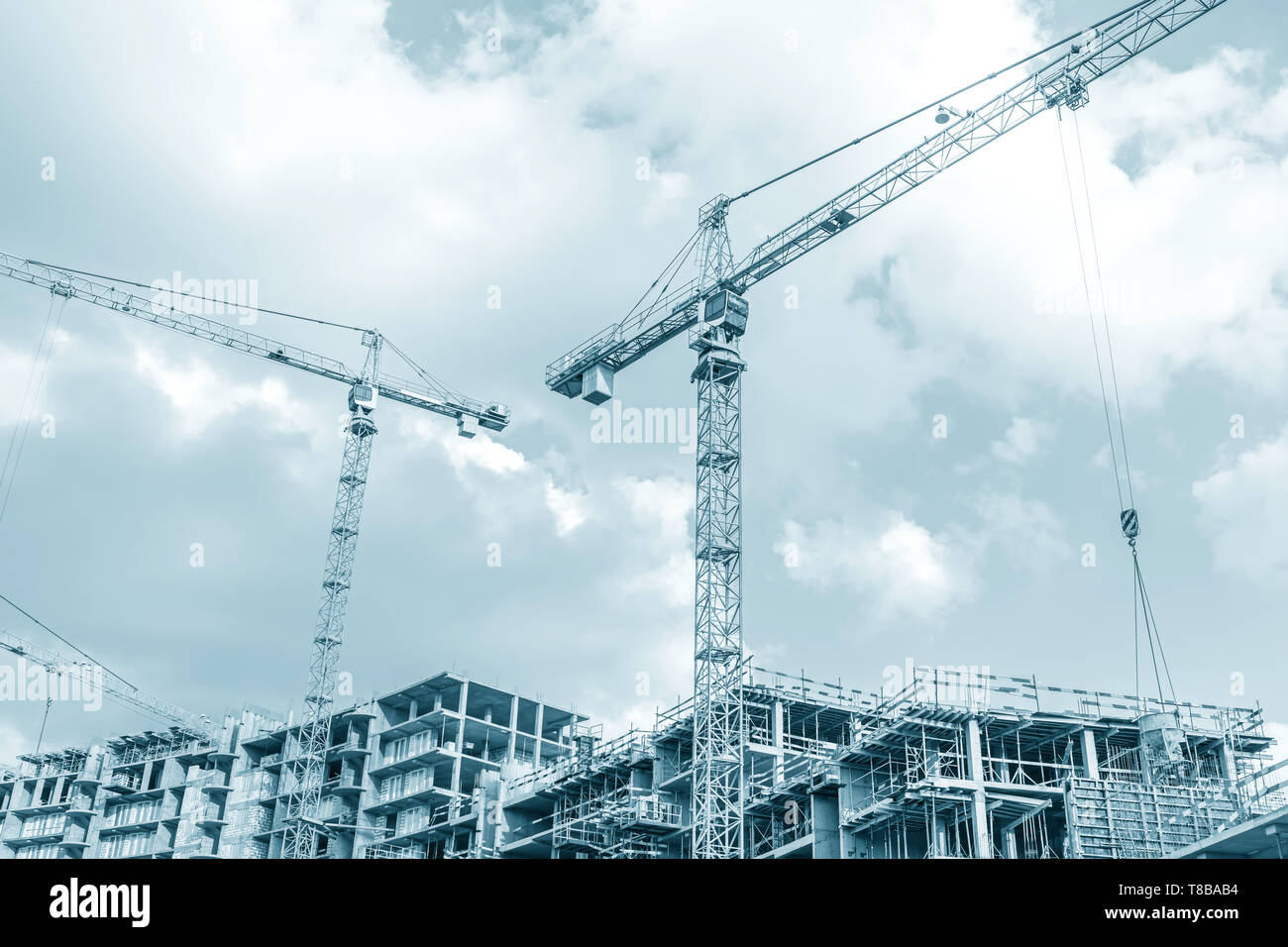 Gru a torre in città sito in costruzione contro il cielo nuvoloso. Sfondo immagine dai toni Foto Stock