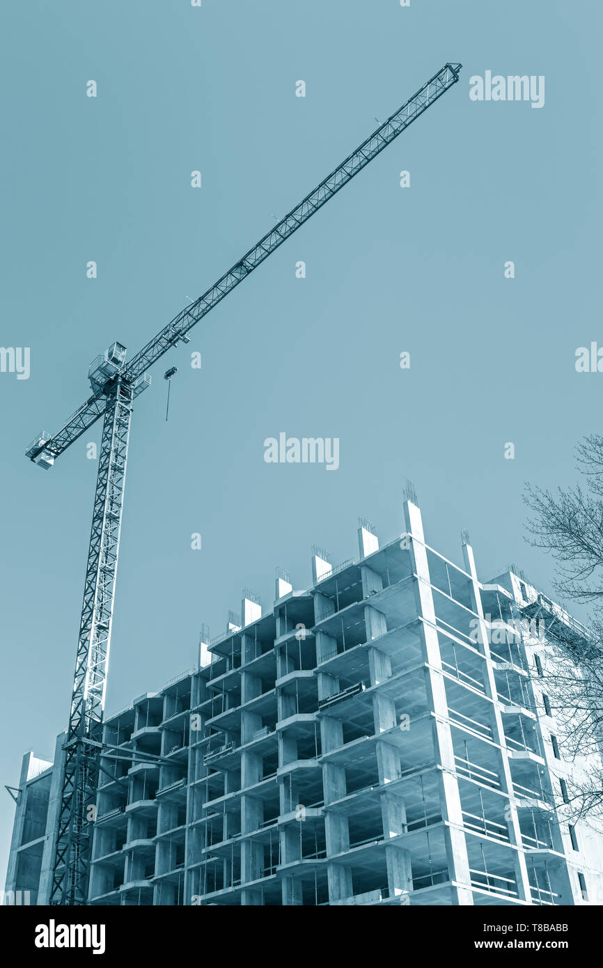 Gru a torre vicino edificio di appartamenti in costruzione contro il cielo blu sullo sfondo. vista dal basso Foto Stock