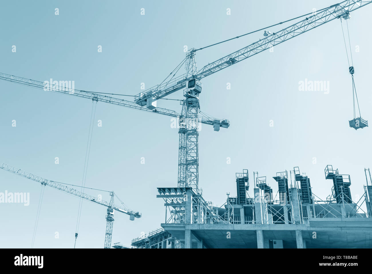 Gru per edilizia lavorando sul sito di costruzione contro il cielo blu sullo sfondo Foto Stock