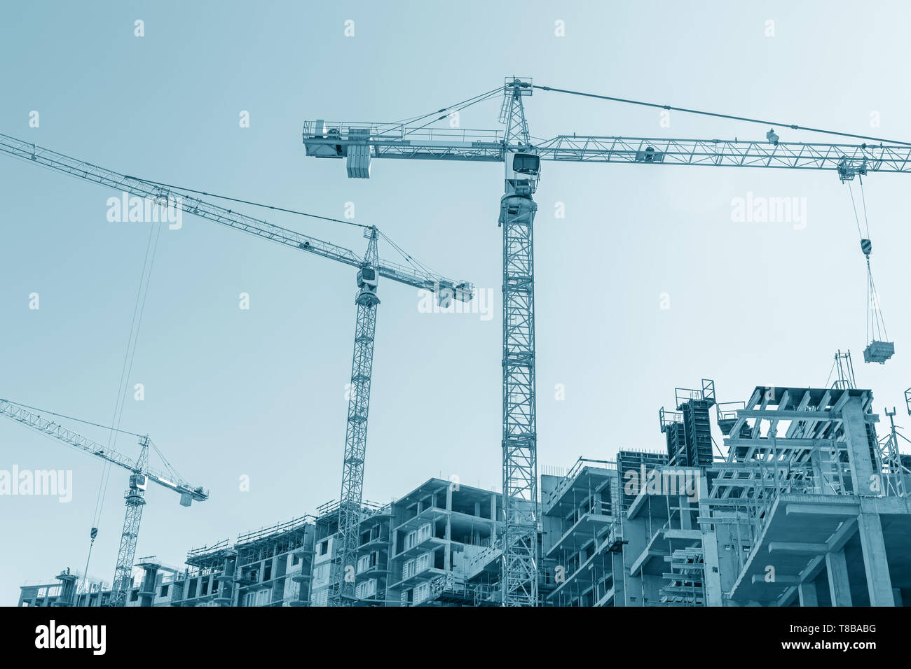 Lo sviluppo della nuova zona della città. gru per edilizia lavorando sul sito di costruzione contro il cielo blu sullo sfondo Foto Stock