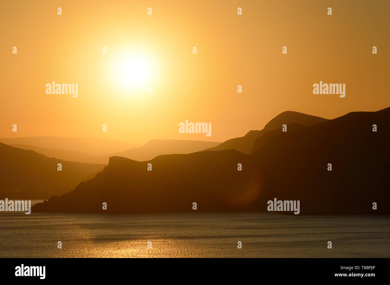 Paesaggio serale presso il mare. Il sole che tramonta dietro alle montagne. Foto Stock