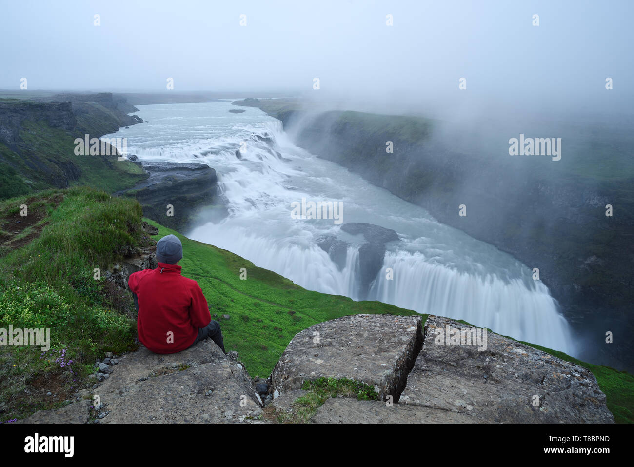 Gullfoss cascata nel canyon di montagna. Attrazione turistica in Islanda. L'uomo turistico in giacca rossa seduta ed esamina il flusso di caduta wate Foto Stock