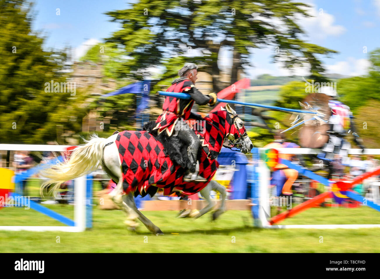 Il cavaliere rosso galoppa lungo il brandeggio verso il suo avversario durante una giostra performance al Castello di Sudeley giostre annuale evento in Winchcombe, nel Gloucestershire. Foto Stock