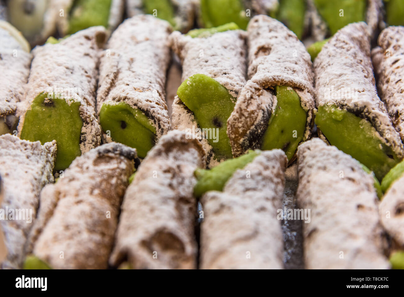 File di cannoli italiani ai pistacchi freschi spolverati di zucchero a velo in esposizione in una panetteria a Napoli, Italia. Pasticceria napoletana tradizionale. Foto Stock
