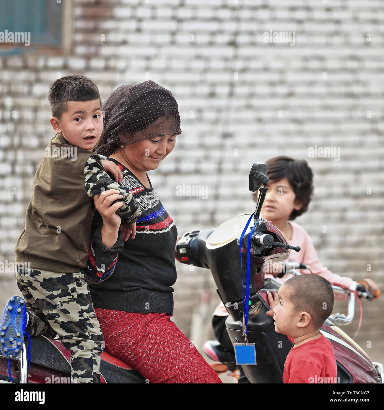 Uyghur madre e figlio a guidare il loro scooter. Hotan-Xinjiang-Cina-0133 Foto Stock