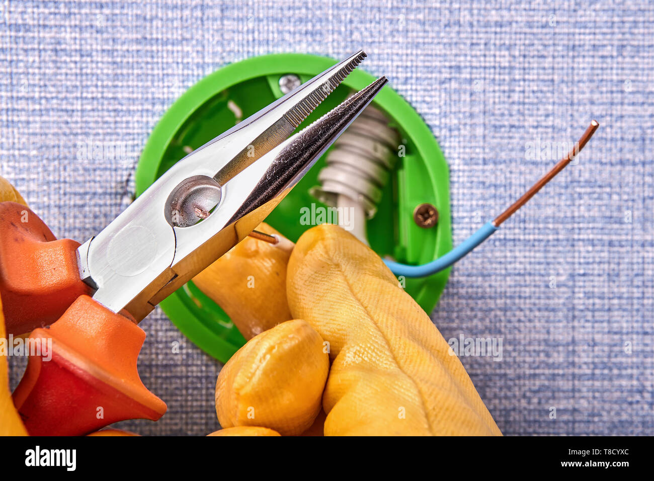 Elettricista in guanti di protezione è il taglio delle estremità dei fili di uscita rotondo scatola con pinze a becchi lunghi, installazione elettrica. Foto Stock