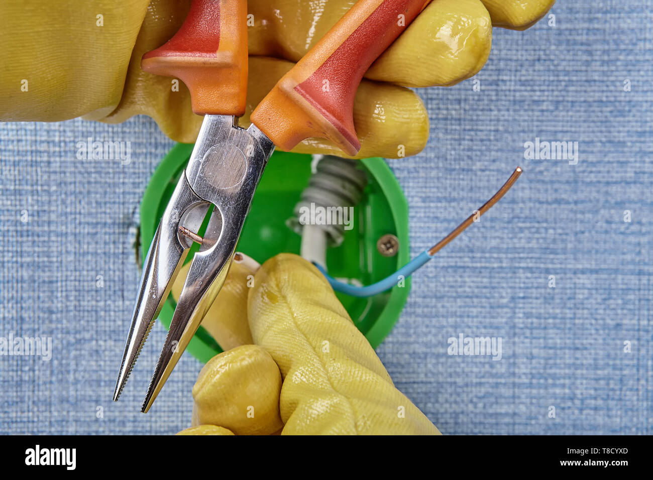 Lavoratore di guanti protettivi è il taglio delle estremità del cablaggio in rame di round della scatola elettrica con pinze a becchi mezzotondi, lavoro elettrico. Foto Stock
