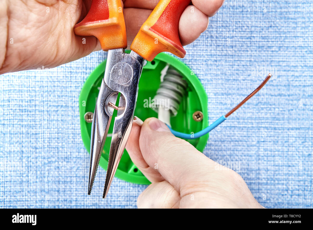 Lavoratore è l'installazione di un nuovo round casella di uscita il taglio di cavi in rame con lo strumento Mano, manutenzione elettrica. Foto Stock