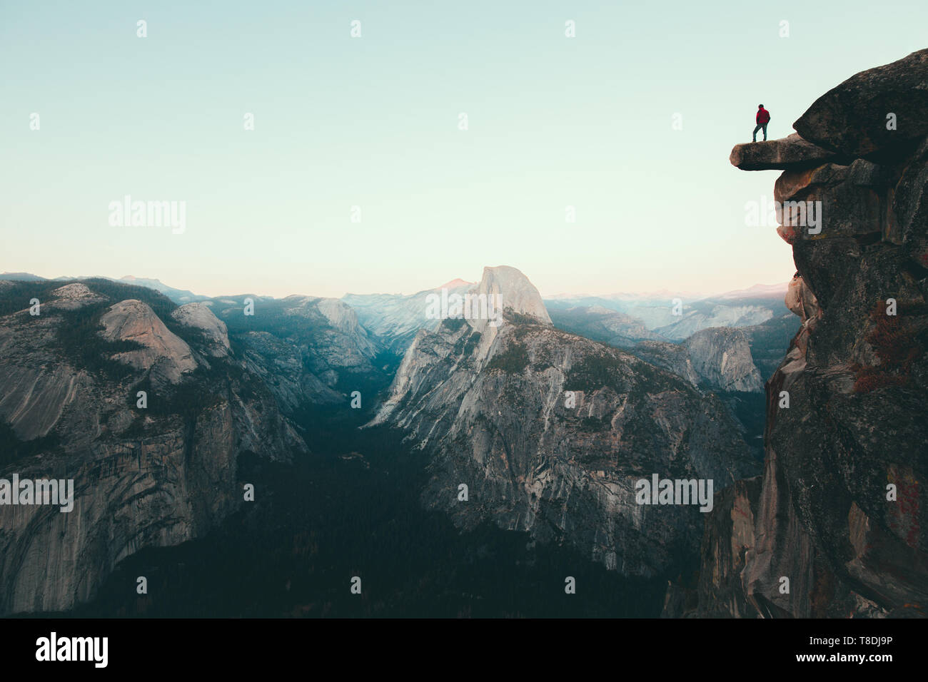 Un intrepido escursionista è in piedi su una roccia a strapiombo godendo della vista verso il famoso Half Dome presso il Glacier Point si affacciano nella bellissima crepuscolo serale Foto Stock