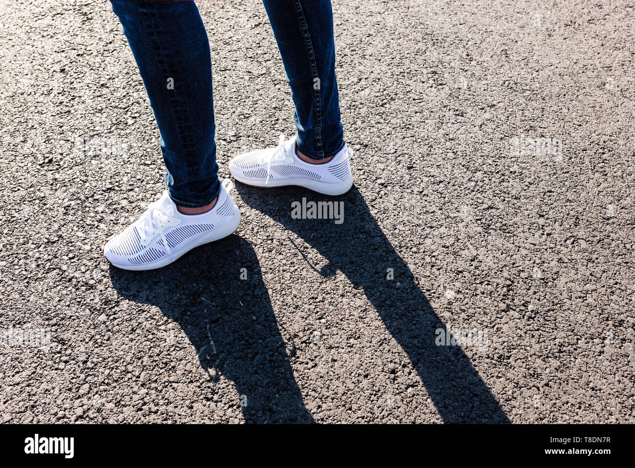 La donna in bianco sneakers permanente sulla strada asfaltata verso il sole, vicino. Foto Stock