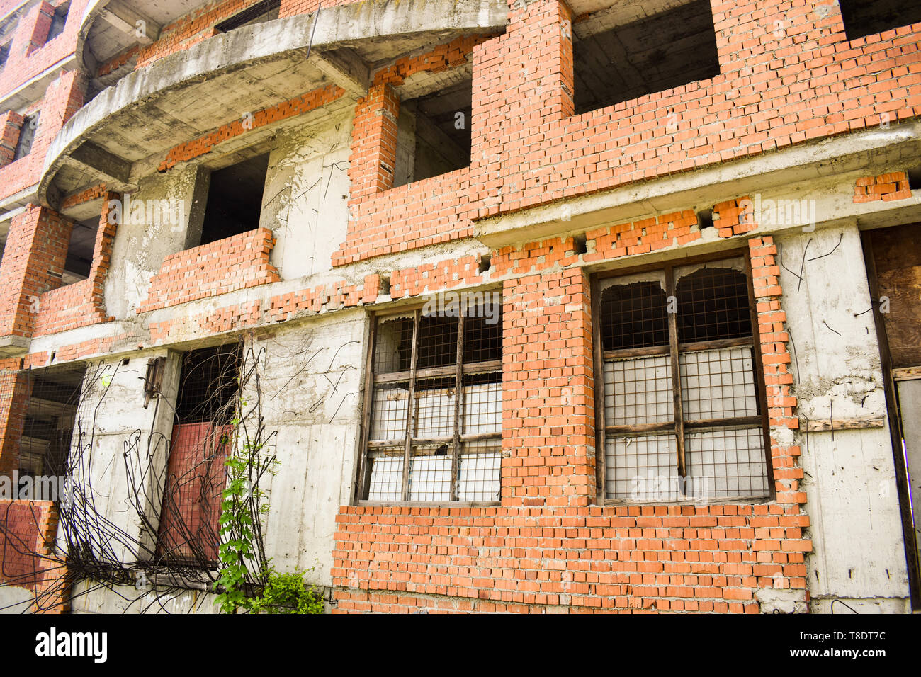 Edificio incompiuto nel centro cittadino. Edificio abbandonato progetto con mattoni rossi e vegetazione selvatica Foto Stock