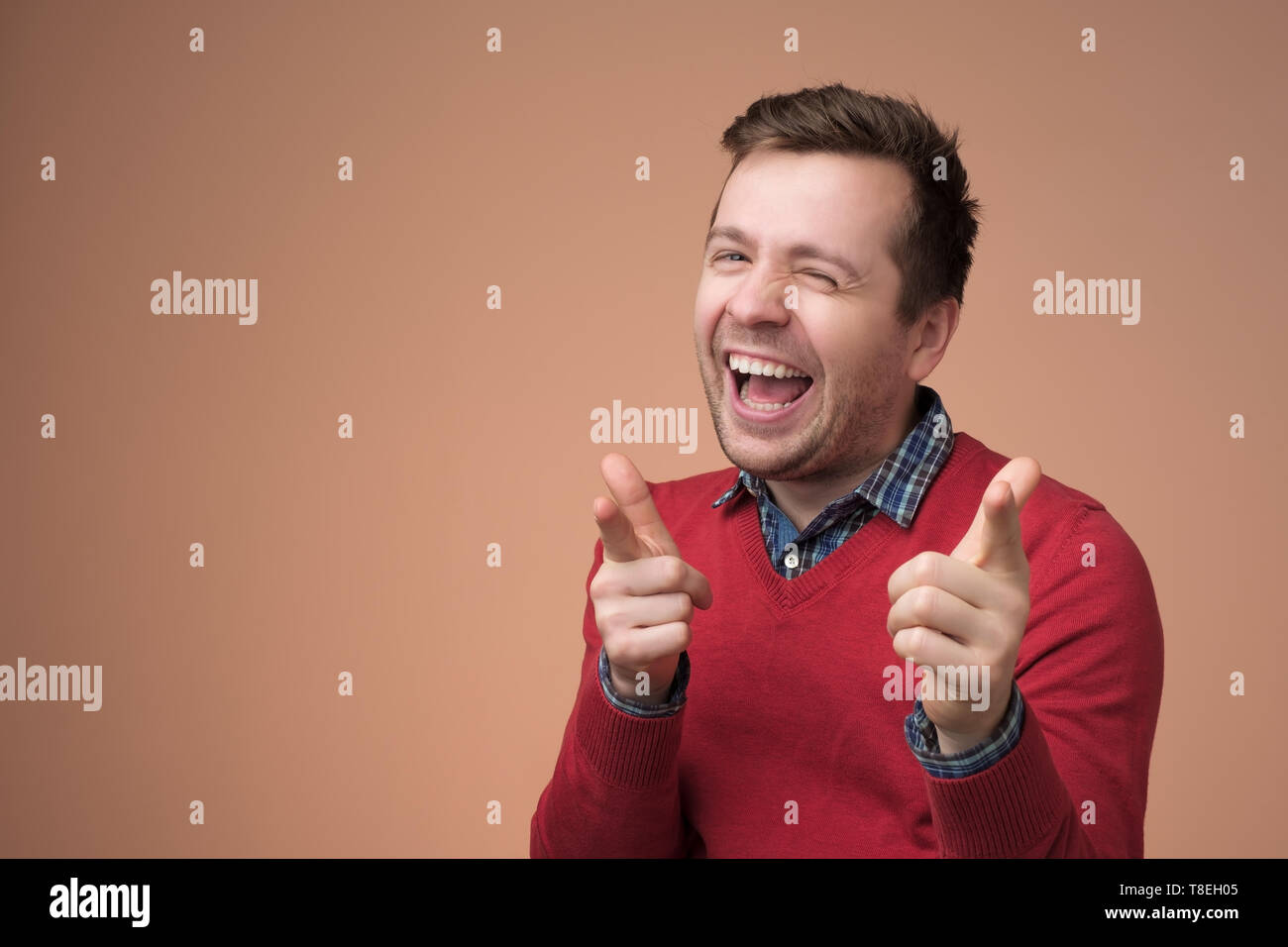 Europeo per il giovane uomo in maglione rosso ridere sul divertente scherzo Foto Stock