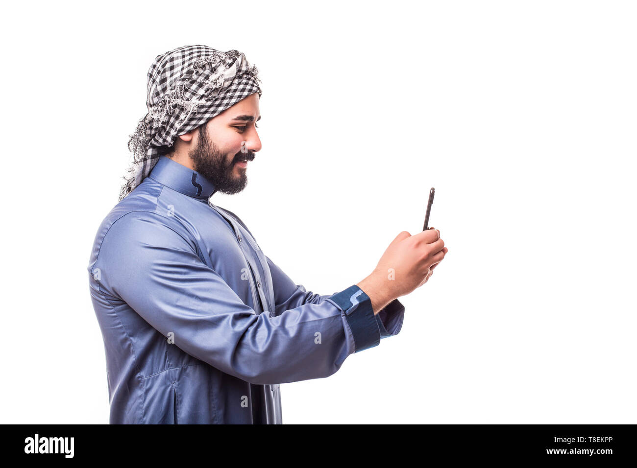 Giovane uomo arabo indossa nel tradizionale abaya vestiti con telefono su sfondo bianco Foto Stock