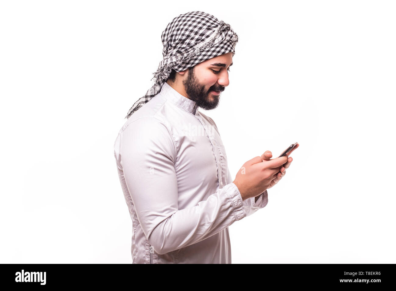 Giovane uomo arabo indossa nel tradizionale abaya vestiti con telefono su sfondo bianco Foto Stock