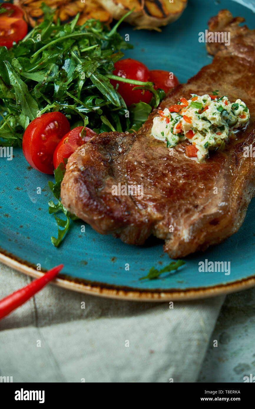 Bistecca con verdure e insalate, con aglio arrostito su una piastra di colore blu e grigio Foto Stock