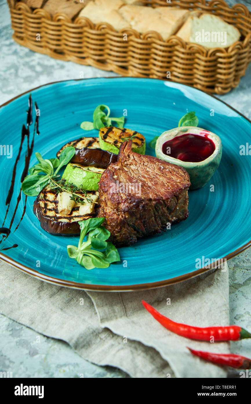 Bistecca con verdure grigliate e salsa di lingonberry su una piastra di colore blu e grigio Foto Stock