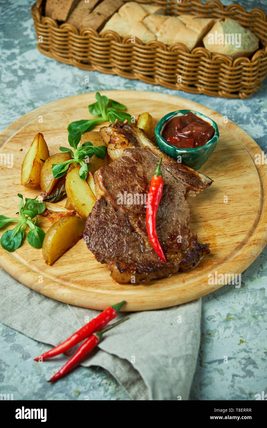 Lombo di osso con patate e basilico, salsa rossa, su una tavola di legno e lo sfondo grigio Foto Stock
