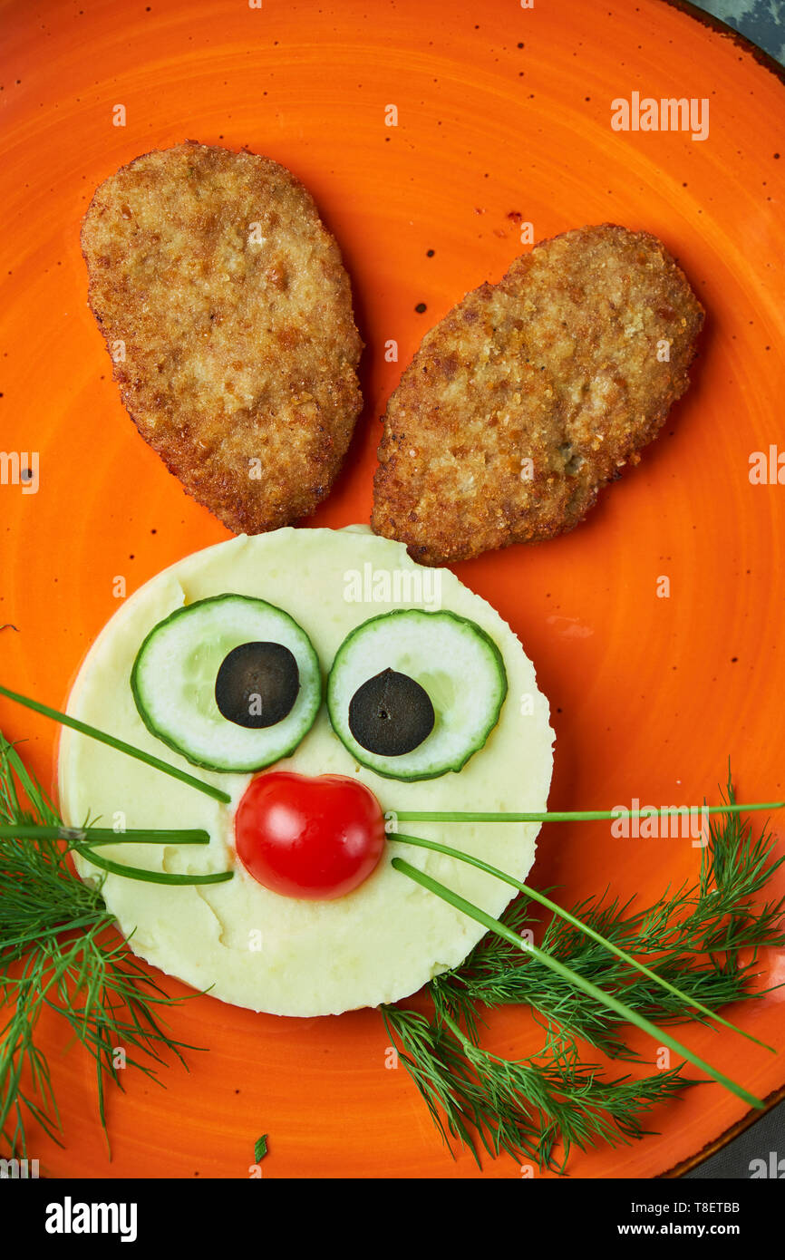 Menu bambini, cotolette con purè di patate sotto forma di una lepre è di testa su una piastra di colore arancione su sfondo grigio Foto Stock