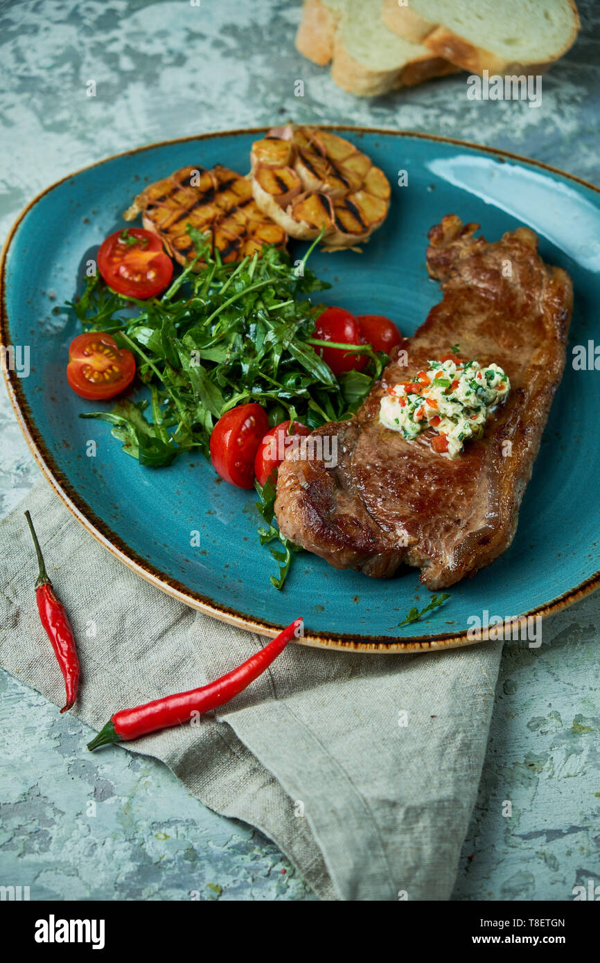 Bistecca con verdure e insalate, con aglio arrostito su una piastra di colore blu e grigio Foto Stock