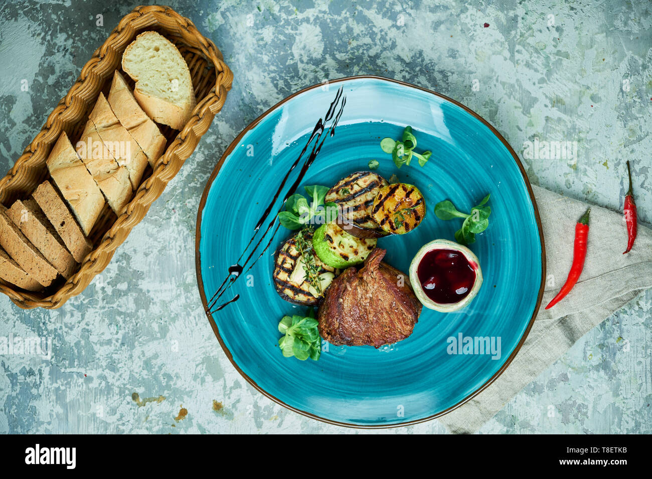 Bistecca con verdure grigliate e salsa di lingonberry su una piastra di colore blu e grigio Foto Stock