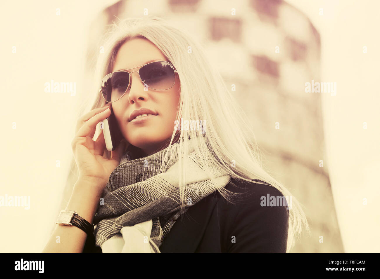 Blonde business donna in occhiali da sole utilizzando il telefono cellulare all'aperto a piedi elegante modello di moda indossando blazer nero e grigio sciarpa Foto Stock