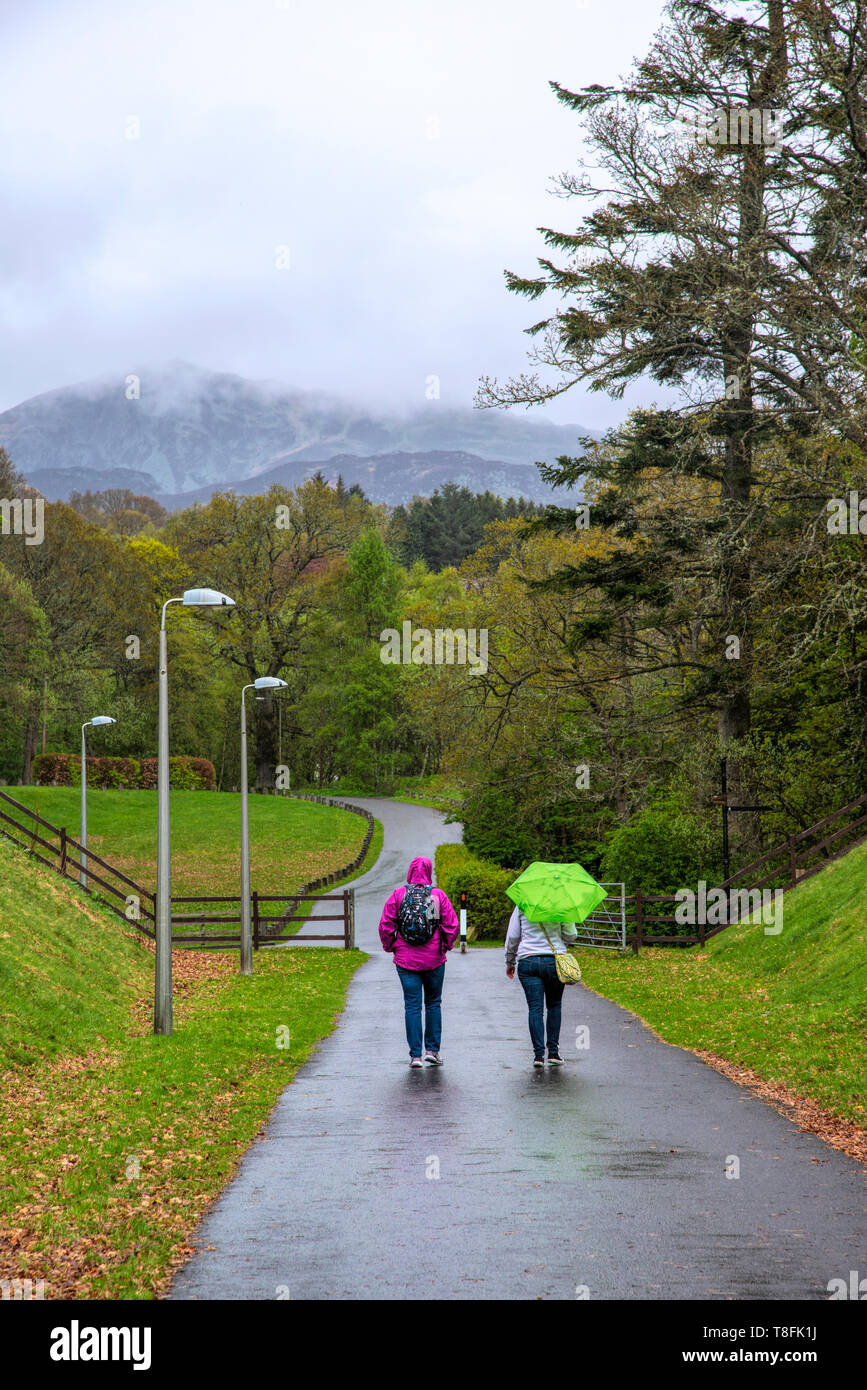 Due persone a piedi attraverso un parco sotto la pioggia. Pitlochry, Scozia. Foto Stock