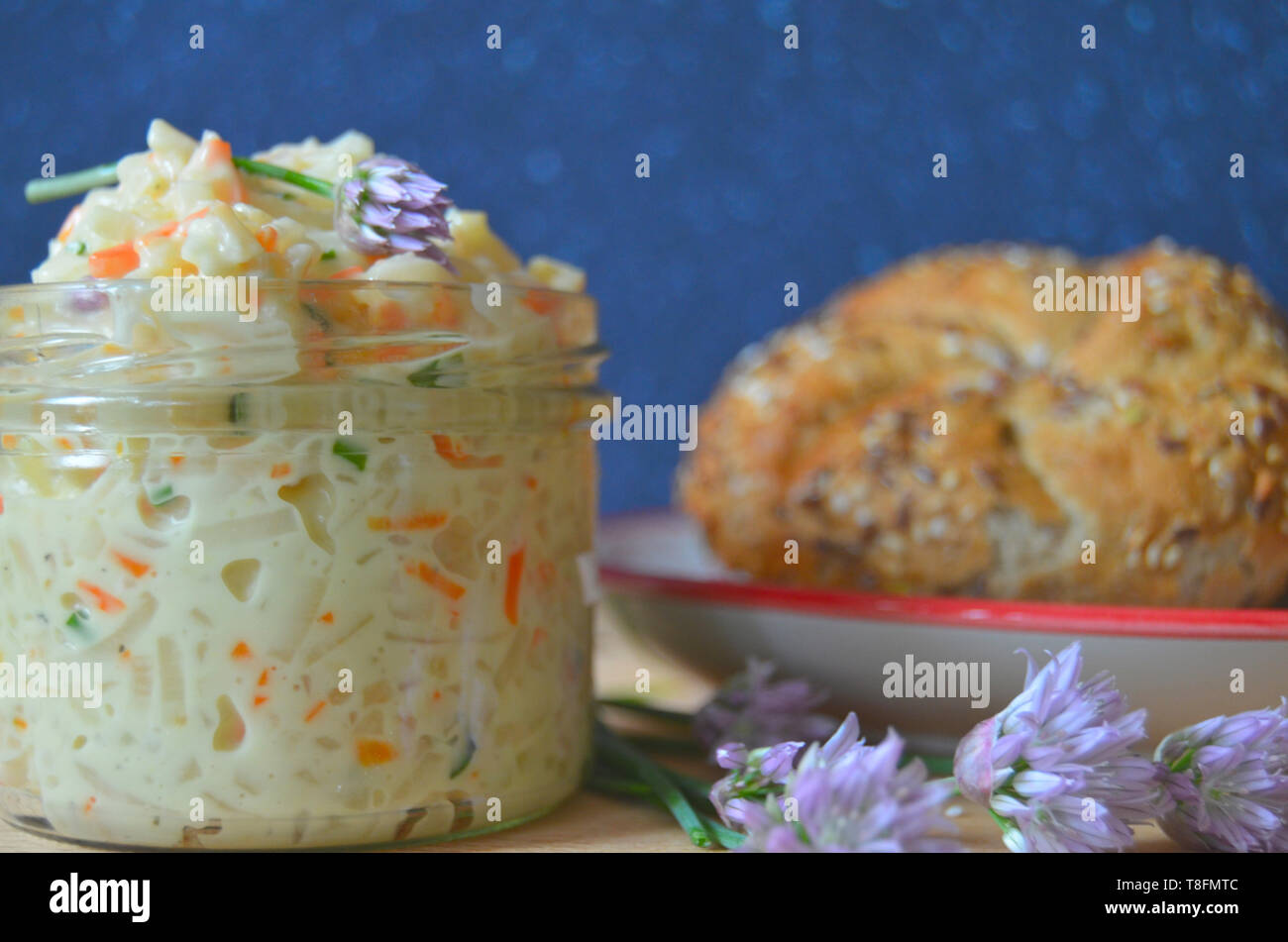 Cibo ceco: shredded sedani rapa e mayo con Insalata di carote e erba cipollina in un vaso, decorato con fiori di erba cipollina, con un kaiser bun in background Foto Stock