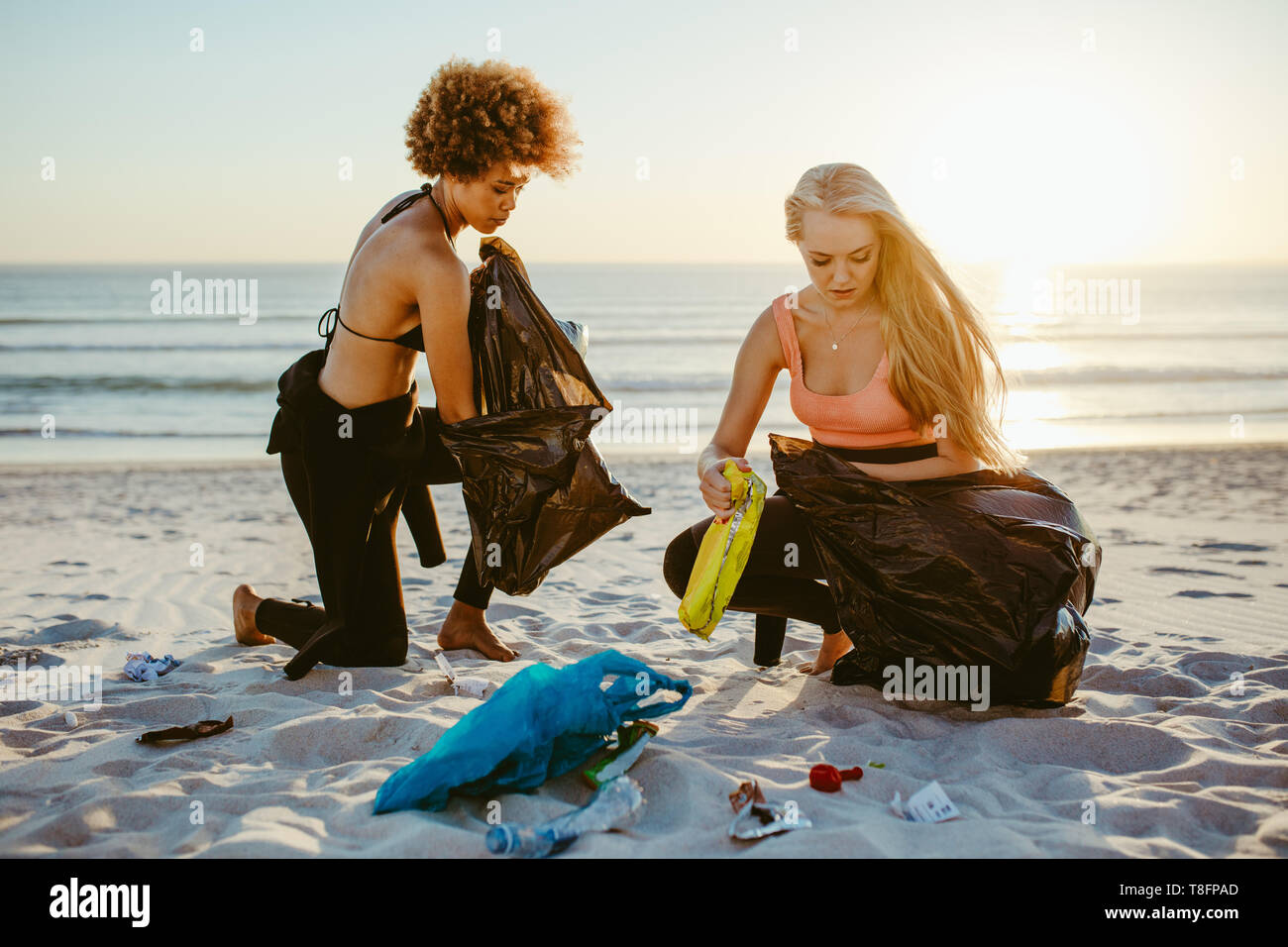 Due giovani donne di prelevare i rifiuti dalla spiaggia. Surfista femmina la pulizia della spiaggia, la raccolta dei rifiuti nel sacchetto di immondizia. Foto Stock