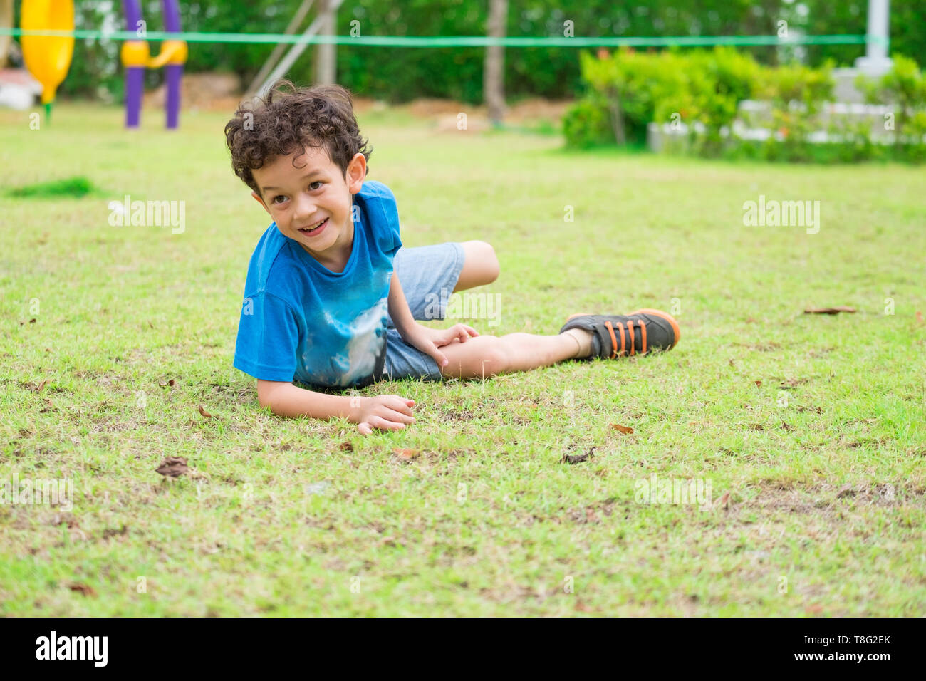 Kid boy divertirsi a giocare un'area giochi per bambini a scuola,kid in esecuzione e cadere sull'erba.torna a scuola l'attività all'aperto. Foto Stock