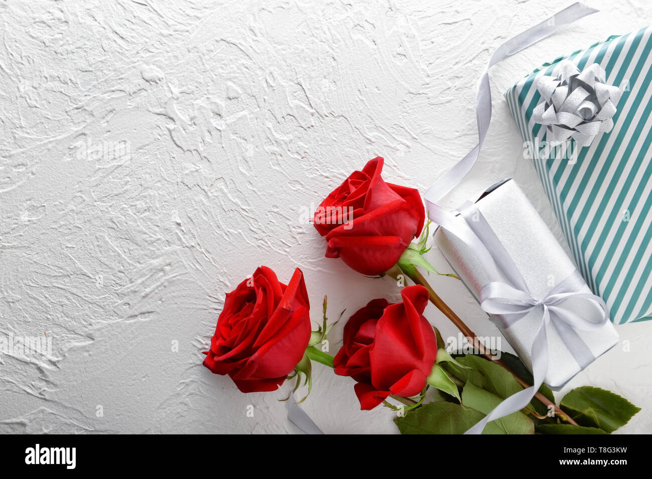 Bellissime rose rosse e confezioni regalo su sfondo chiaro Foto Stock