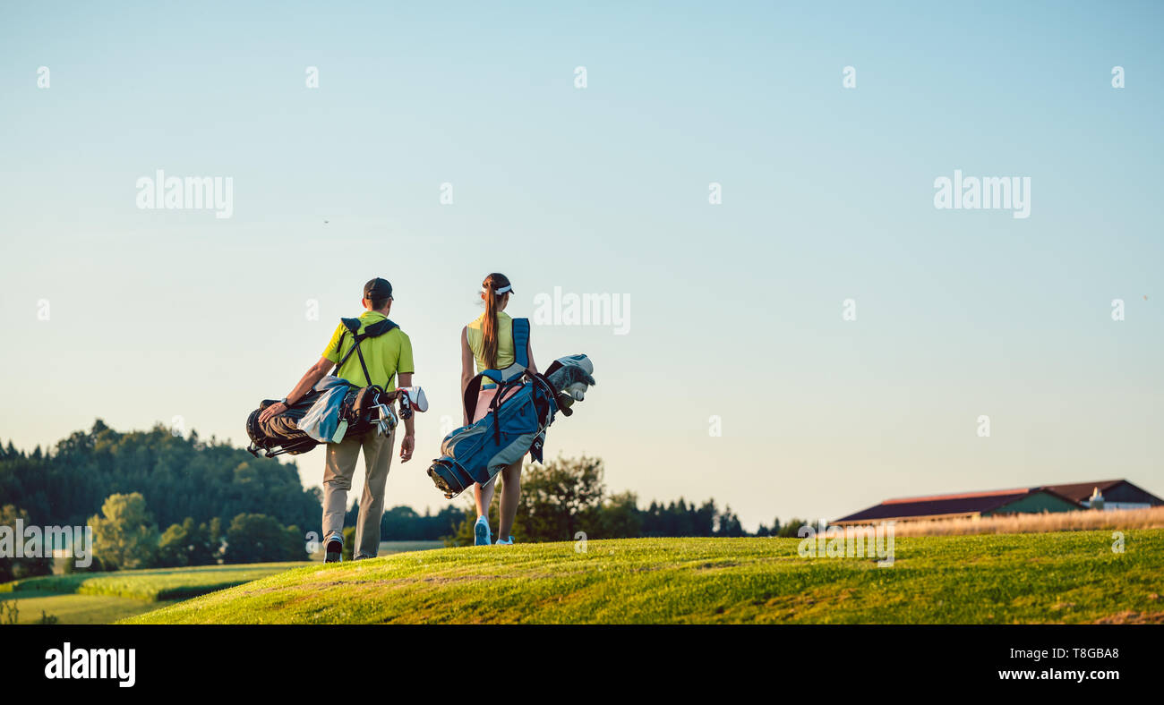 Coppia felice che trasportano stand sacchi verso il campo da golf in una giornata di sole Foto Stock