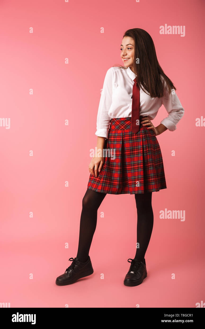 Ritratto di ragazza positiva 15-16y in uniforme scolastica in piedi isolato su sfondo rosso Foto Stock