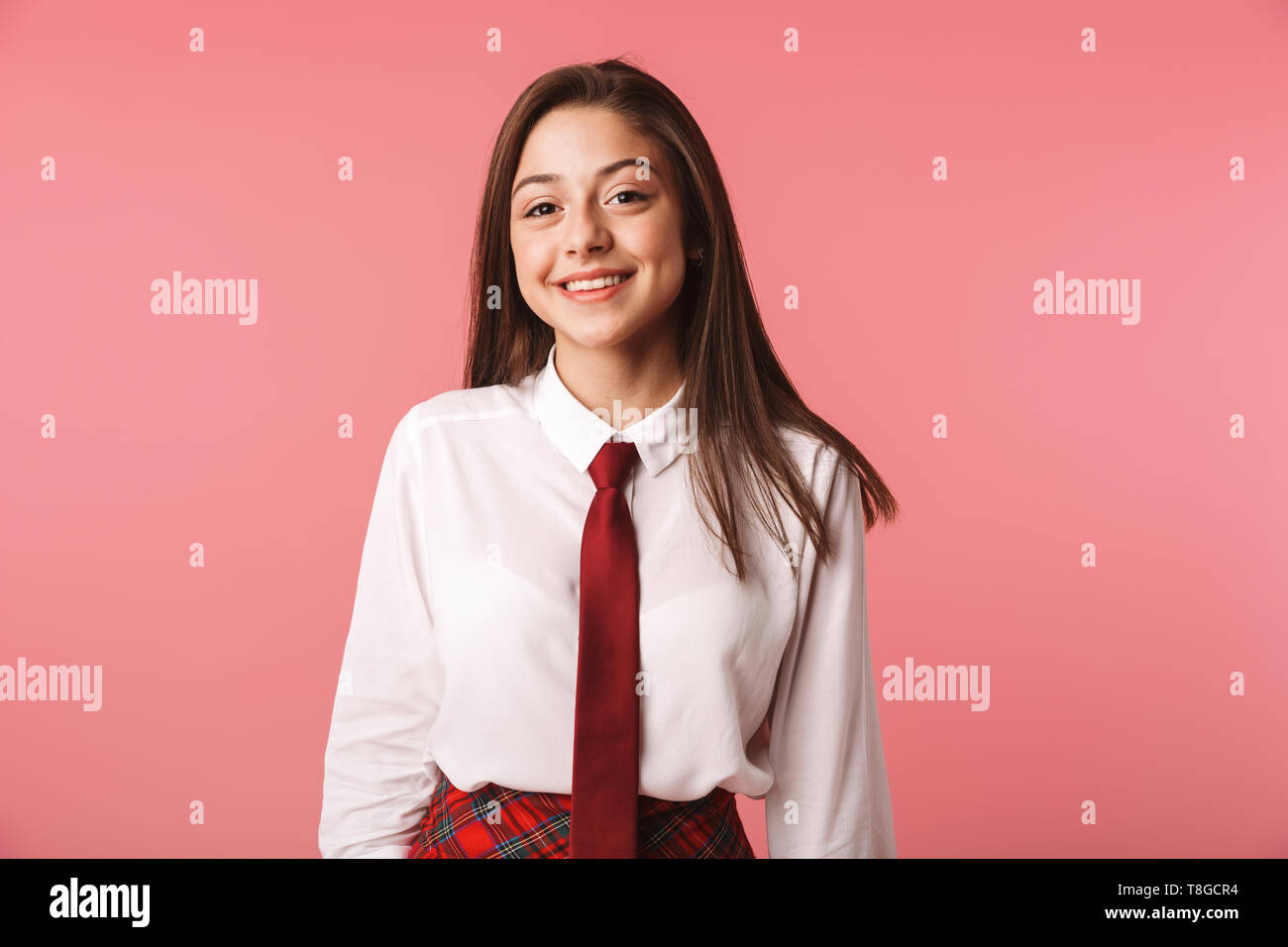 Ritratto di brunette girl 15-16y in uniforme scolastica in piedi isolato su sfondo rosso Foto Stock
