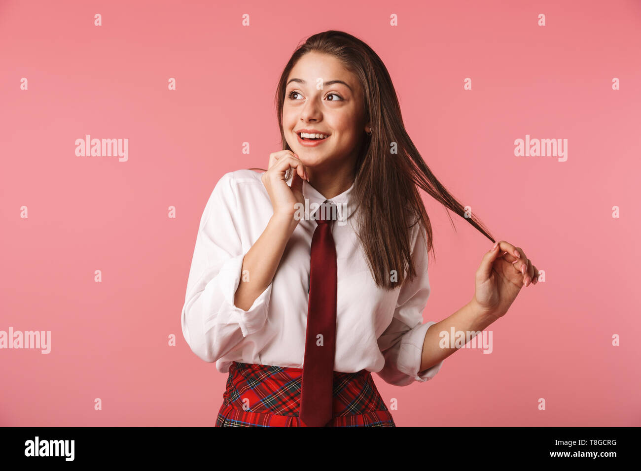 Ritratto di felice ragazza 15-16y in uniforme scolastica in piedi isolato su sfondo rosso Foto Stock
