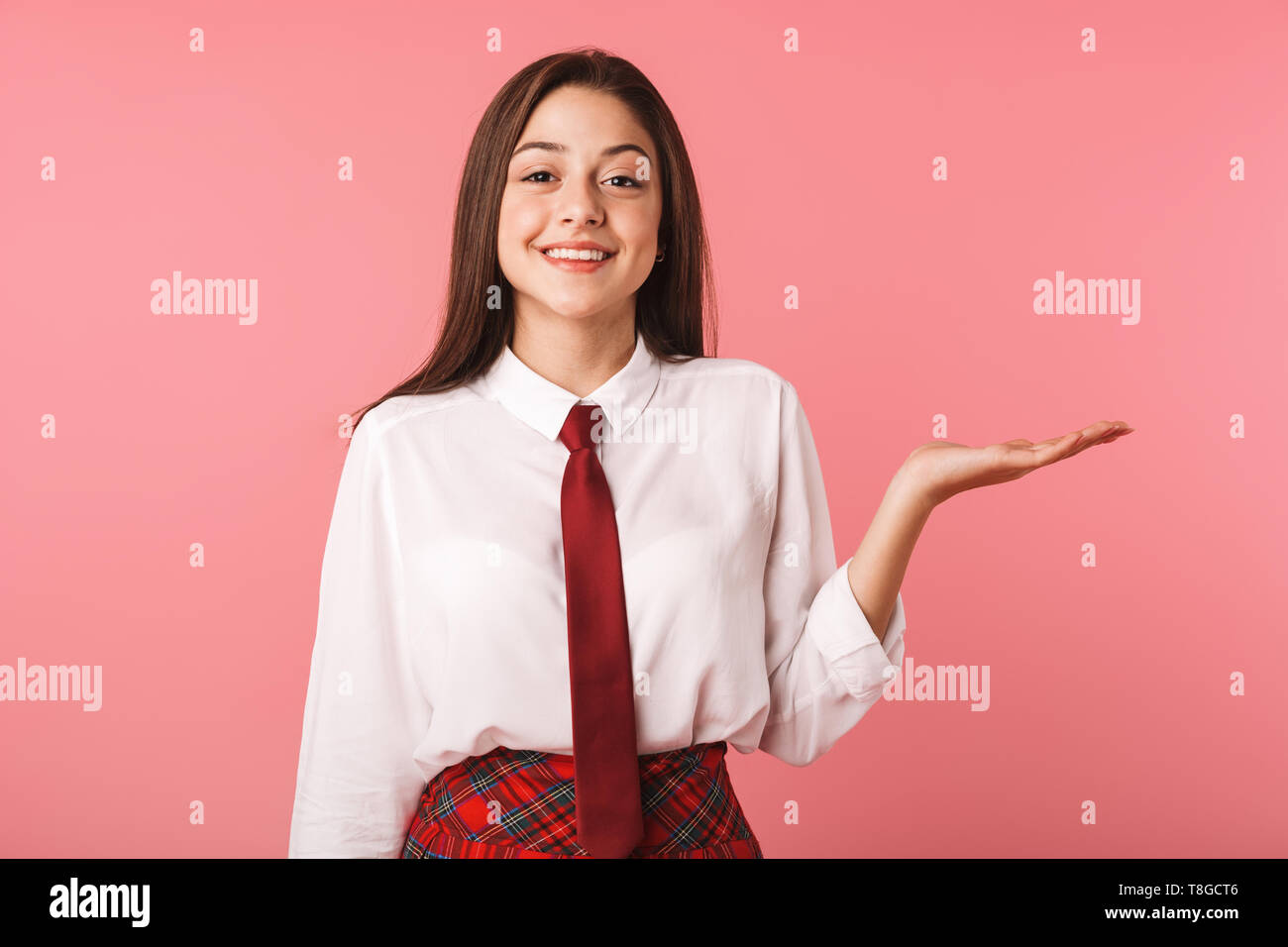 Immagine della ragazza felice 15-16y in uniforme scolastica in piedi isolato su sfondo rosso Foto Stock