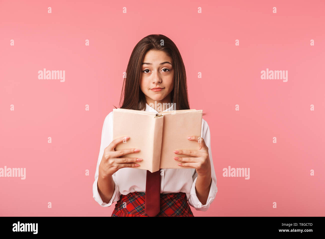 Ritratto di bella ragazza 15-16y in uniforme scolastica libro di lettura permanente, mentre isolate su sfondo rosso Foto Stock